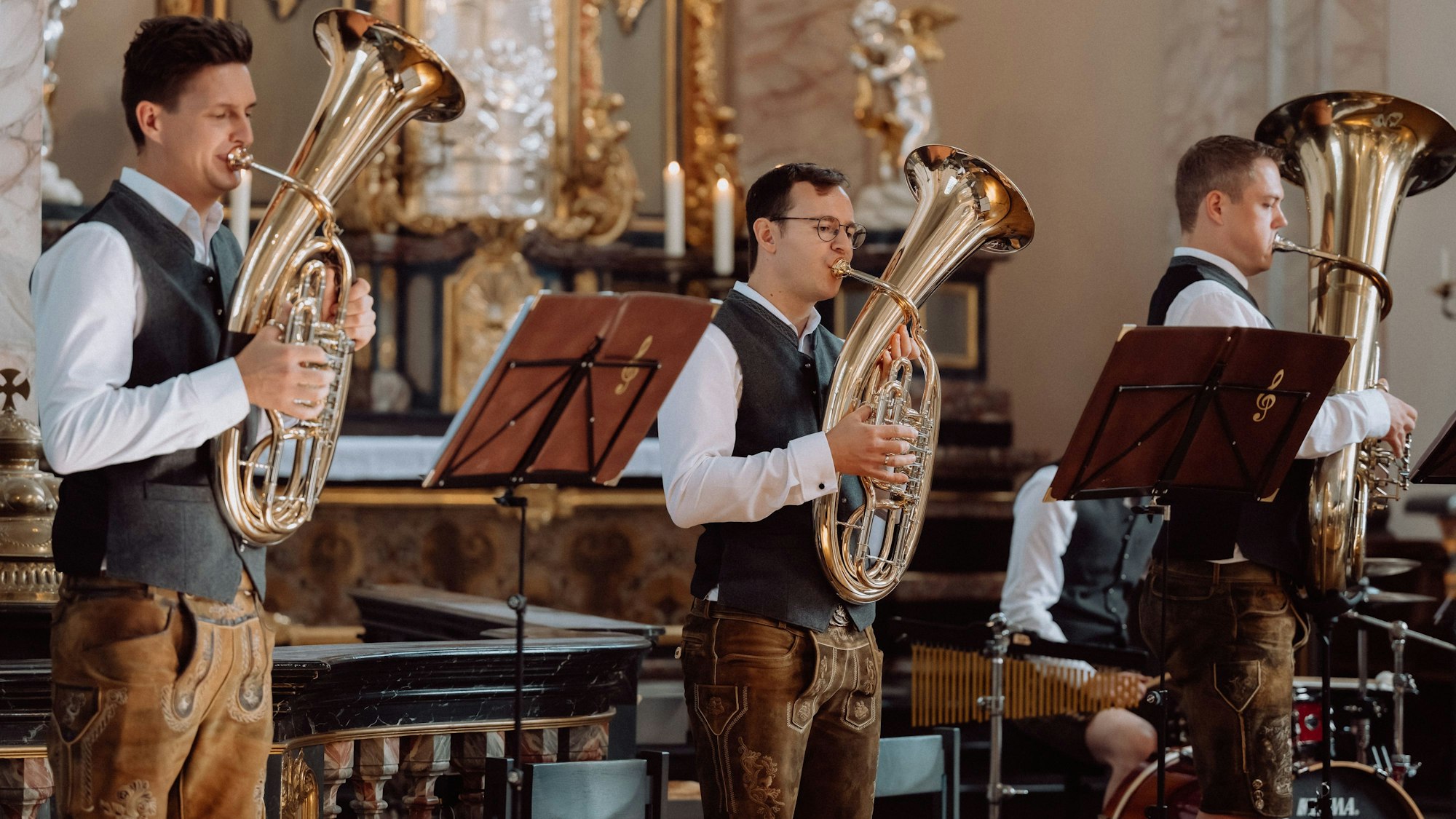 Drei Musiker der Band Blechformat im Trachtenlook beim Auftritt in einer Kirche.