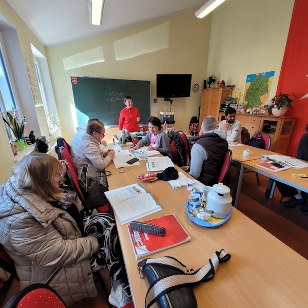 Frauen und Männer im Deutschunterricht, im Hintergrund die Lehrerin Iris Braun.