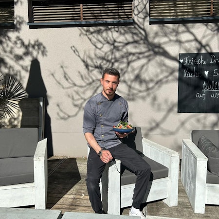 Ein Mann sitzt mit einem Teller Salat vor dem Sportcenter Kautz in Köln-Klettenberg.