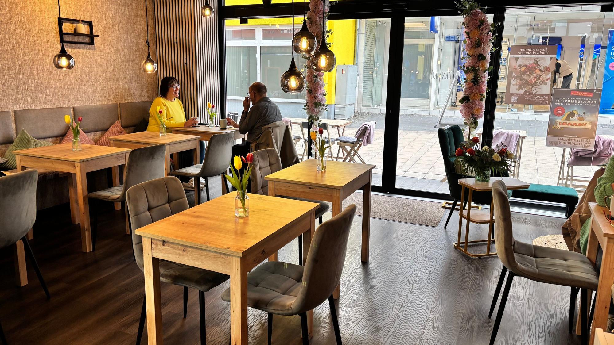 Das Foto zeigt einen kleinen Café-Raum. Links an der großen Fensterfront sitzen zwei Frauen.