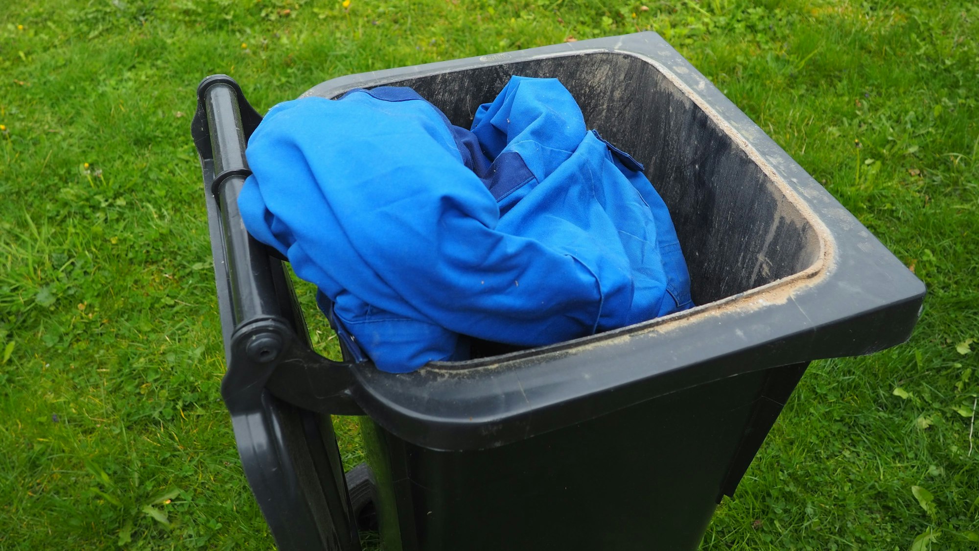 In einer aufgeklappten Restmülltonne liegt eine blaue Jacke.