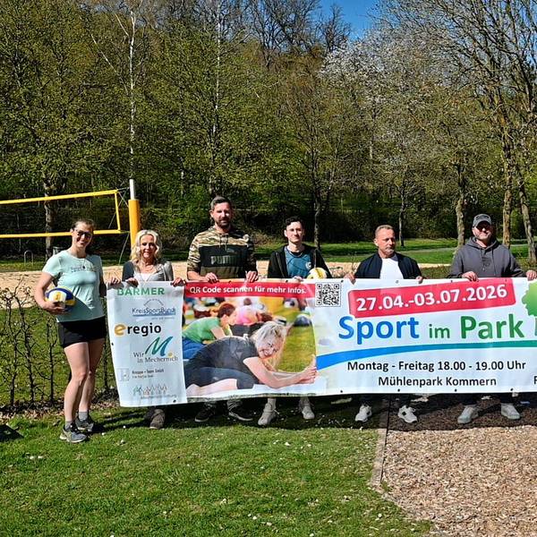 Im Mechernicher Mühlenpark stehen Mitglieder des Organisations- und Trainerteams hinter einem Banner, der das „Sport im Park“-Projekt bewirbt.