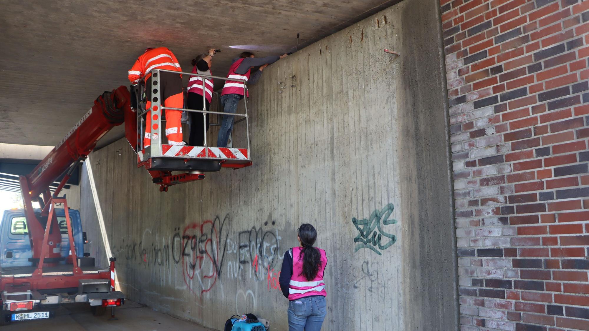 Menschen stehen im Tragekorb eines Hubwagens unter einem Brückenwerk.