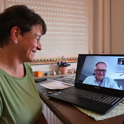 Eine Frau blickt einen Mann auf dem Bildschirm ihres Laptops an, beide lächeln.