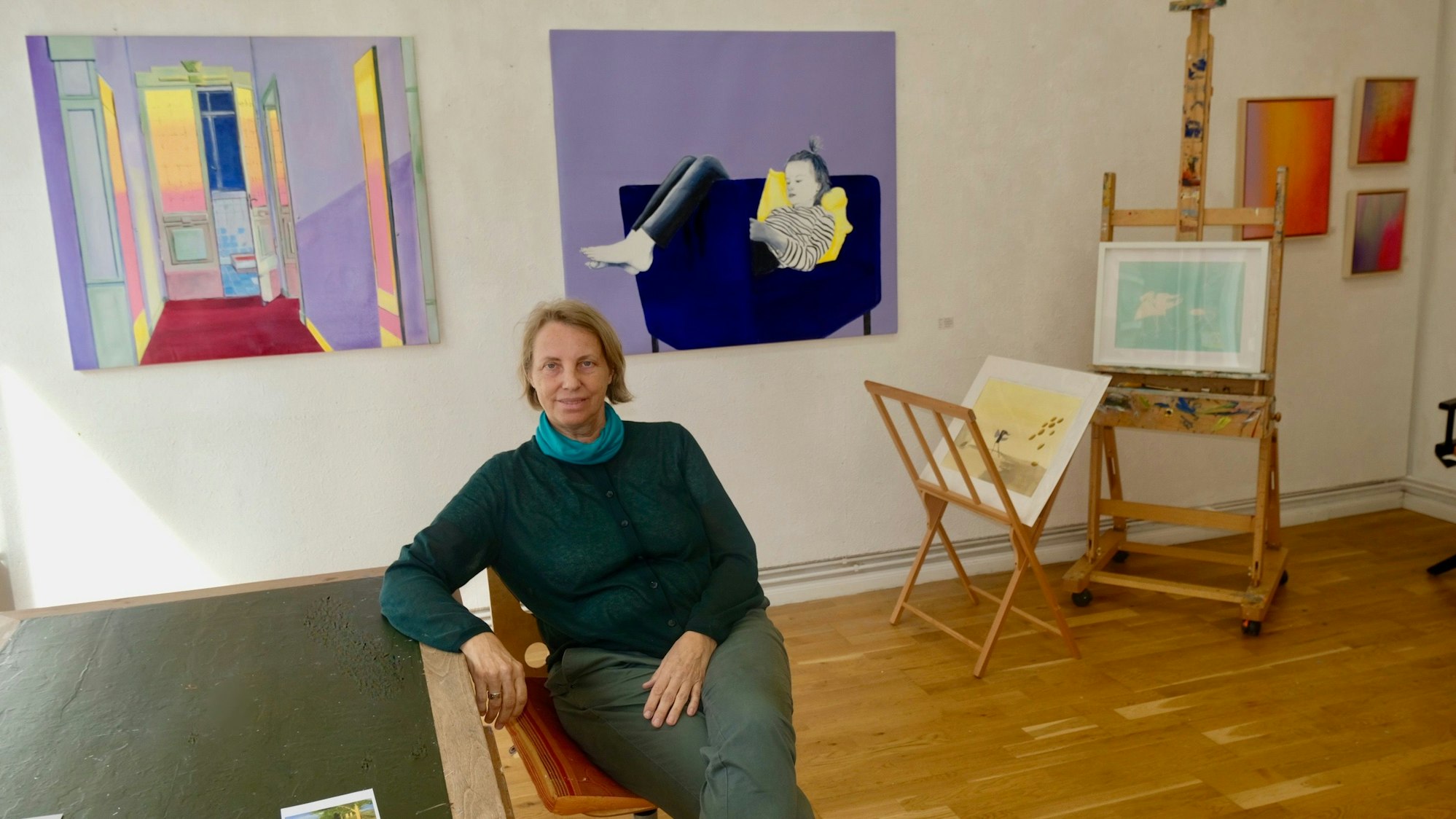 Eine Frau sitzt vor ihren Gemälden im Atelier Köln Süd.