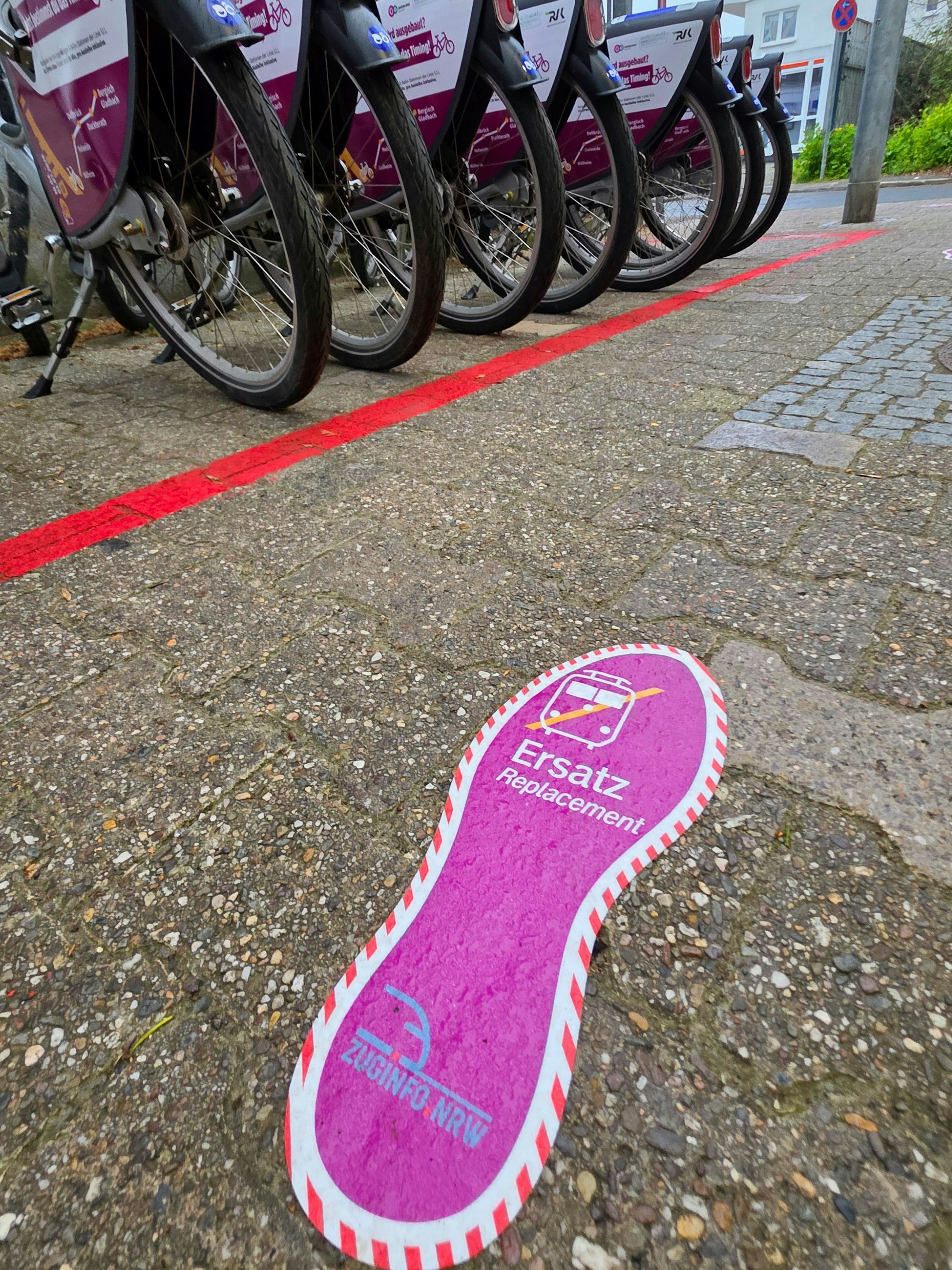 Fußabdruck-Wegweiser zeigen den Weg zu SEV-Haltestelle an der Mülheimer Straße, im Hintergrund stehen SEV-Leihräder.