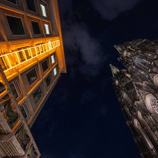 Blick in den dunklen Nachthimmel, gelborange leuchtende Himmelsleiter am Domforum auf der linken Seite, Dom auf der rechten Seite