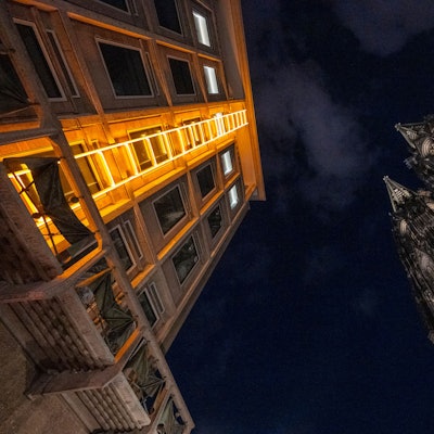 Blick in den dunklen Nachthimmel, gelborange leuchtende Himmelsleiter am Domforum auf der linken Seite, Dom auf der rechten Seite