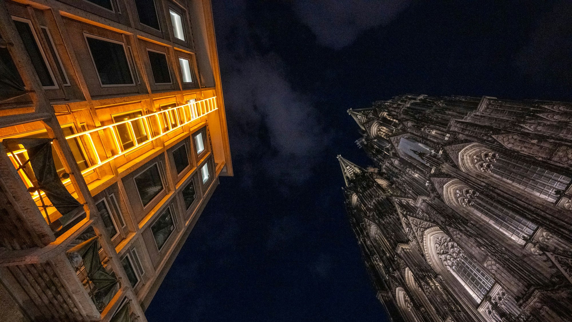 Blick in den dunklen Nachthimmel, gelborange leuchtende Himmelsleiter am Domforum auf der linken Seite, Dom auf der rechten Seite