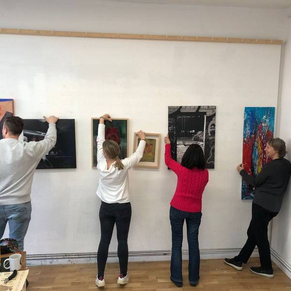 Einige Künstlerinnen und Künstler hängen gemeinsam im Atelier Köln Süd ihre Bilder für eine Ausstellung auf.