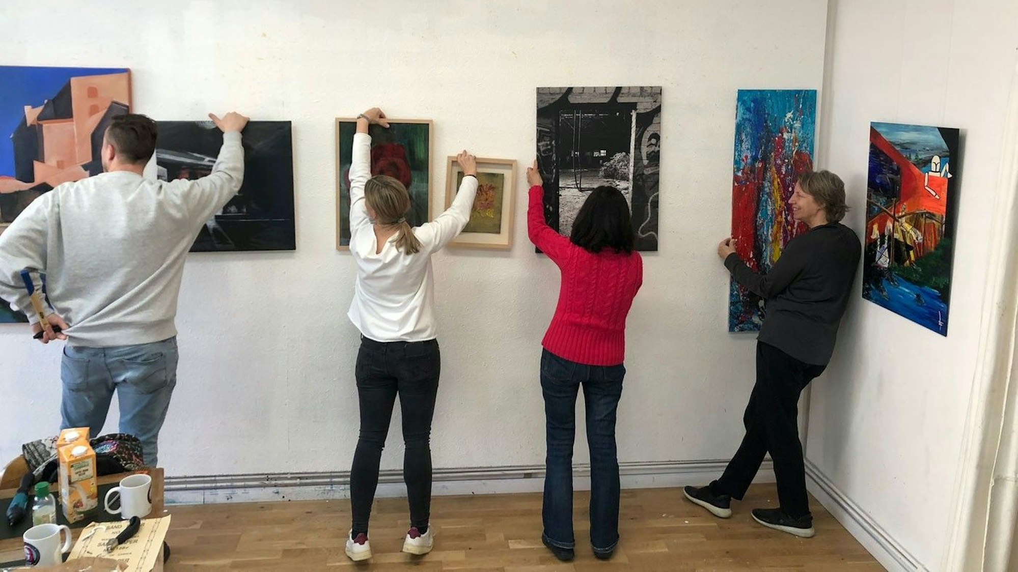 Einige Künstlerinnen und Künstler hängen gemeinsam im Atelier Köln Süd ihre Bilder für eine Ausstellung auf.