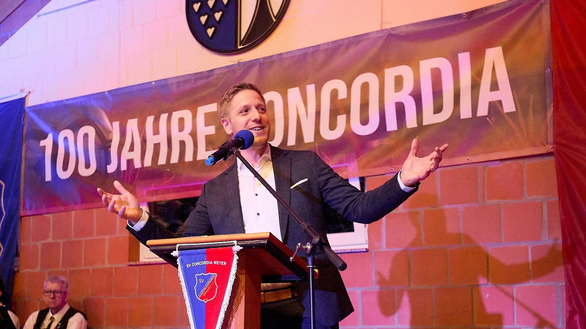 Landrat Markus Ramers steht mit ausgebreiteten Armen am Rednerpult, dahinter der Schriftzug „100 Jahre Concodia“.