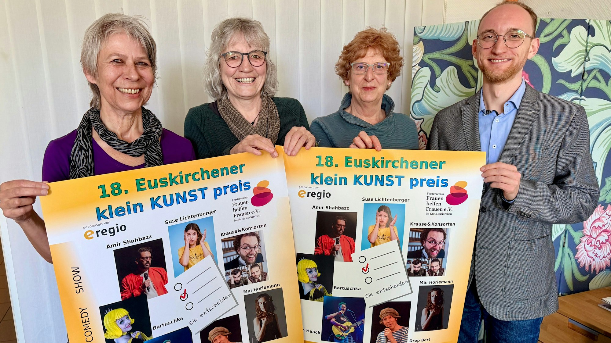 Drei Frauen aus dem Orga-Team und der Vertreter des Hauptsponsors e-regio stehen hinter Plakaten des Kleinkunstpreises und lachen in die Kamera.