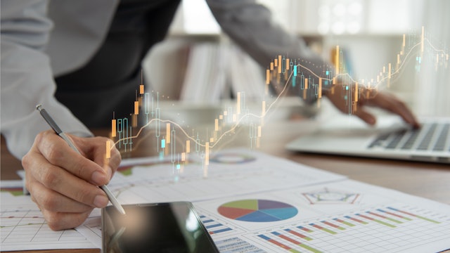 Das Bild zeigt einen Geschäftsmann am Schreibtisch. Auf dem Tisch liegen ausgedruckte Diagramme.