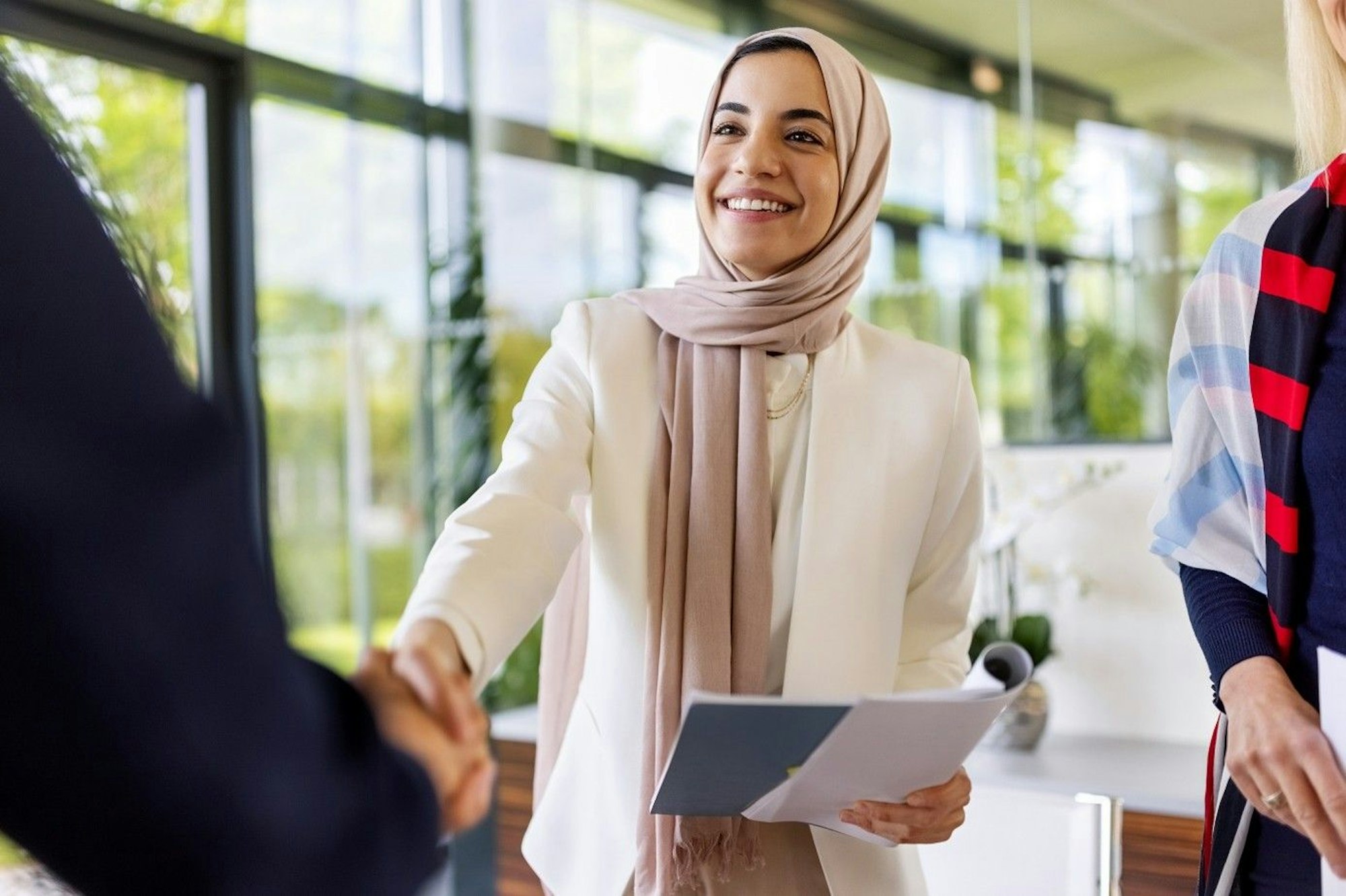 Junge Frau schüttelt einer Person gegenüber die Hand und lächelt. Sie hat Bewerbungsunterlagen in der Hand.