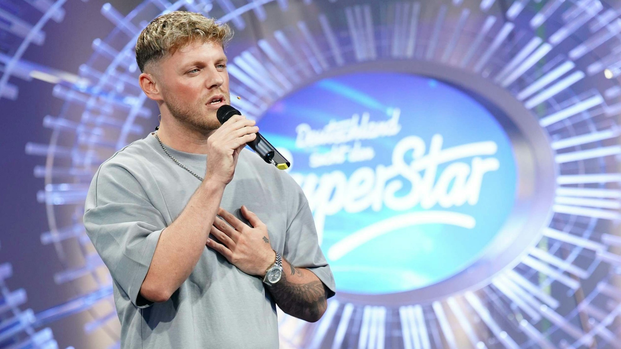 Maric Verch bei seinem Auftritt. Er hält ein Mikro in der Hand und steht vor dem DSDS-Logo.