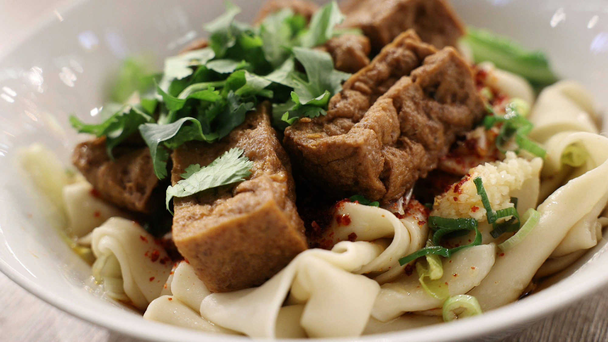 Handgezogene, breite Nudeln, serviert mit Tofu und Kräutern.