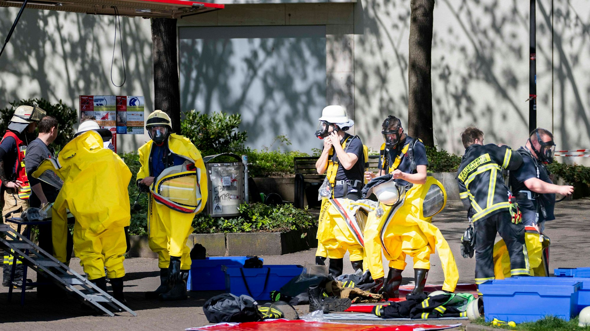 Das Bild zeigt zahlreiche Feuerwehrleute, die im Einsatz sind. Fünf von ihnen ziehen spezielle Schutzanzüge an.