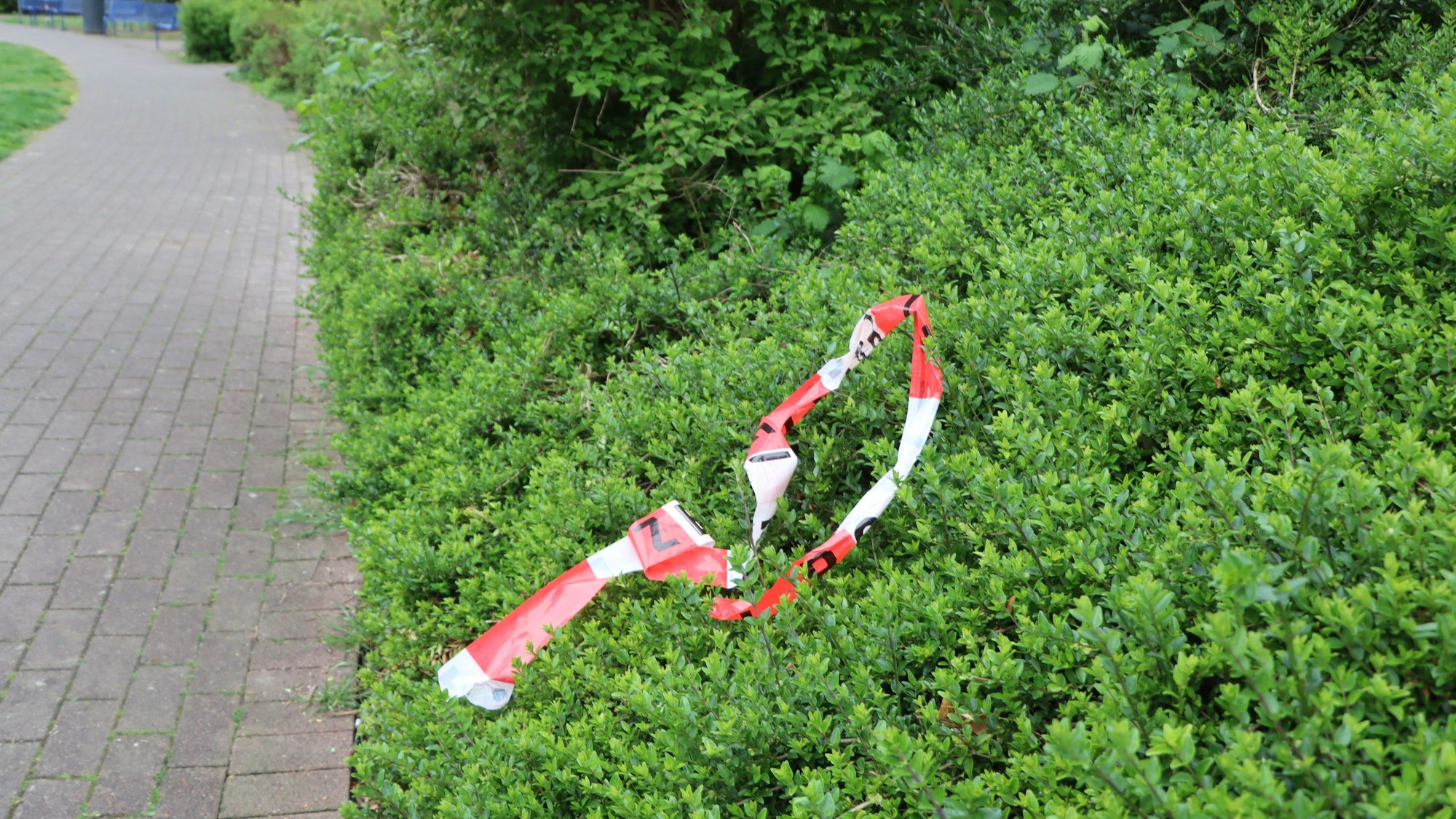 Ein Stück Absperrband liegt in einer Hecke.