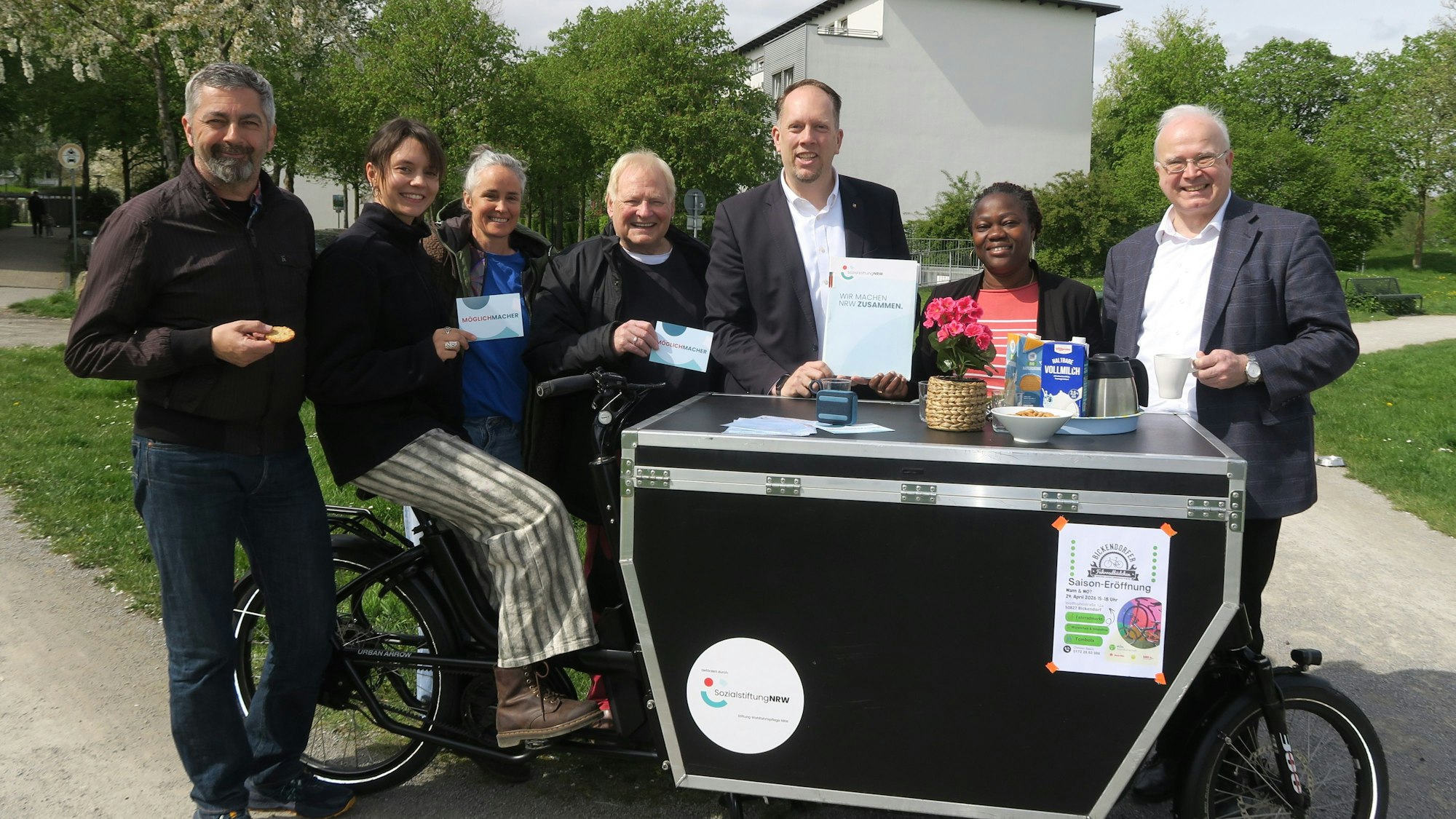 Mehrere Menschen stehen hinter und neben einem zu einem Tisch umgebauten Lastenrad.