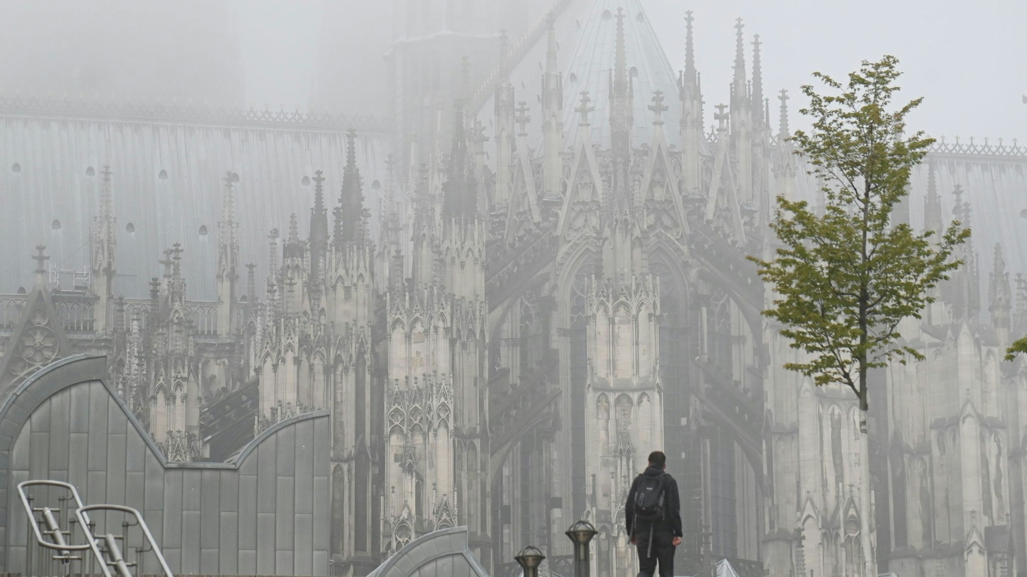 Ein Fußgänger ist am Dienstagmorgen vor dem in Nebel gehüllten Kölner Dom zu sehen.