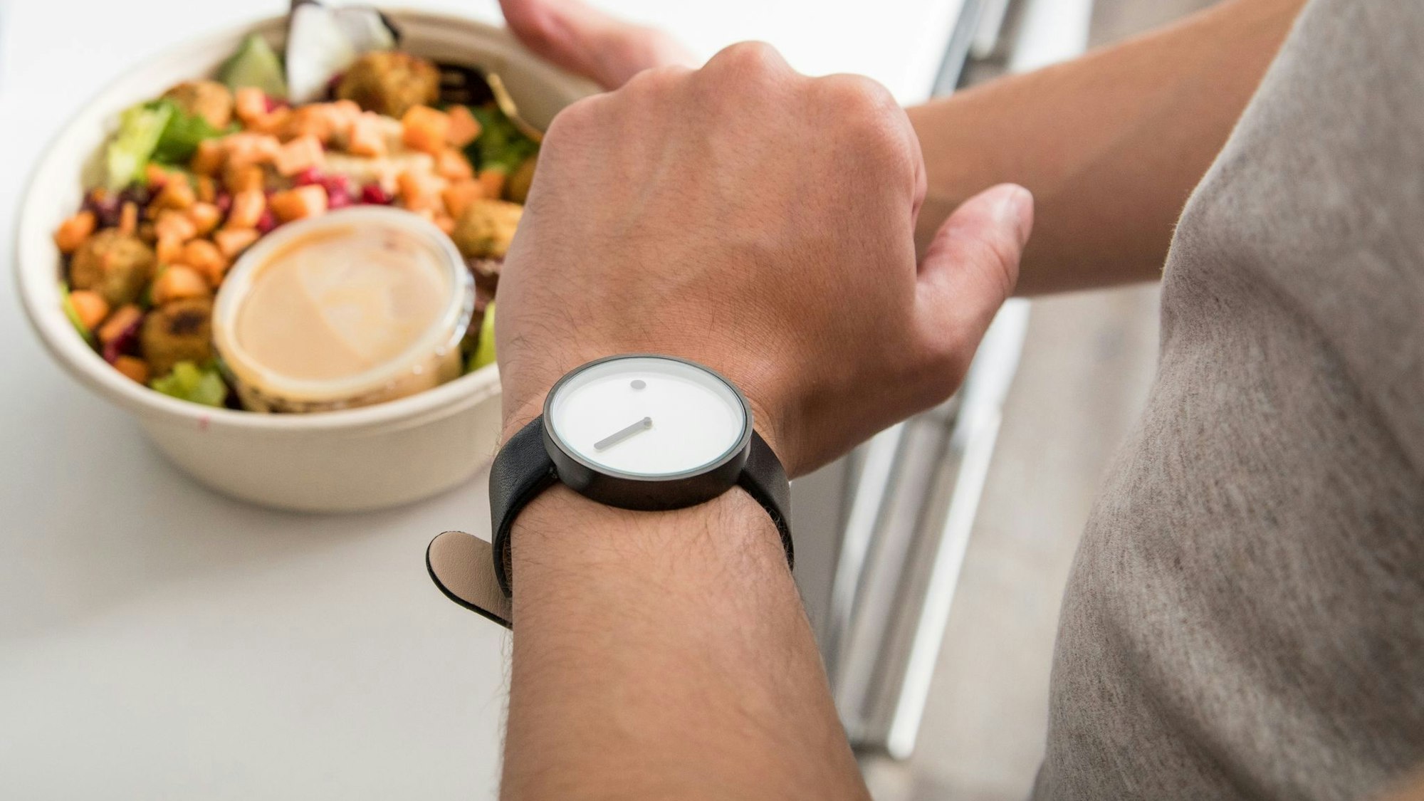 Mann mit einem Salat in der Hand schaut auf seine Armbanduhr