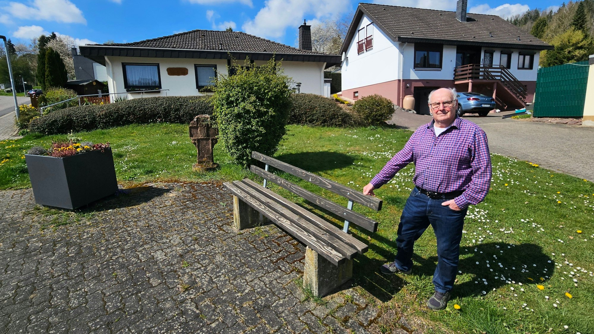 Groß steht neben einer Sitzbank auf einer kleinen Grünanlage.