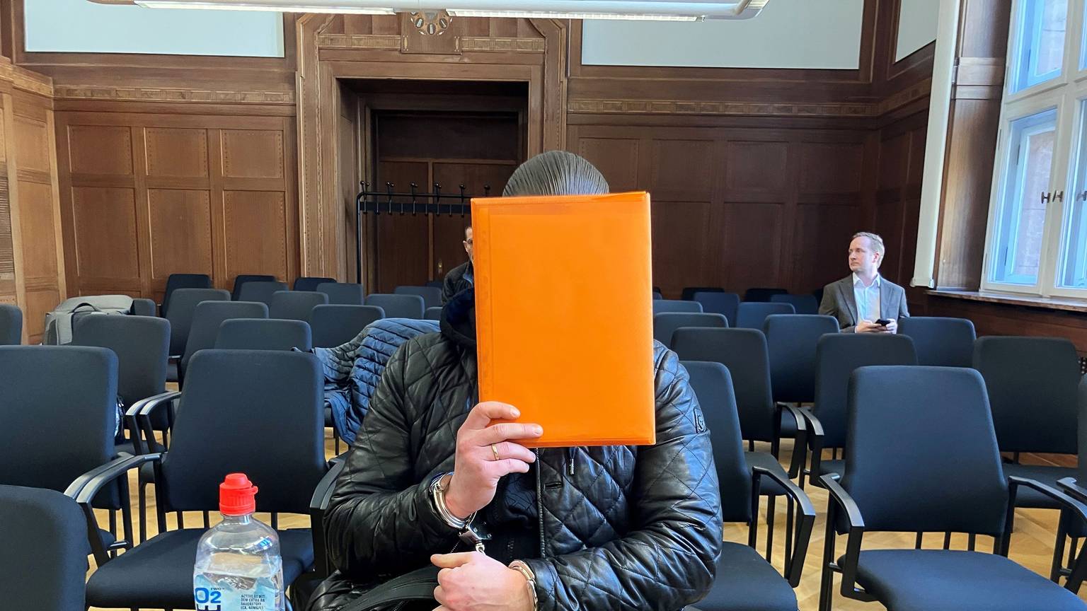Der angeklagte Raser aus Duisburg sitzt im Verhandlungssaal und hält sich eine Mappe vor das Gesicht. Nach einem tödlichem Autorennen verhandelte das Verwaltungsgericht Düsseldorf über die Ausweisung des verurteilten Fahrers in den Kosovo.