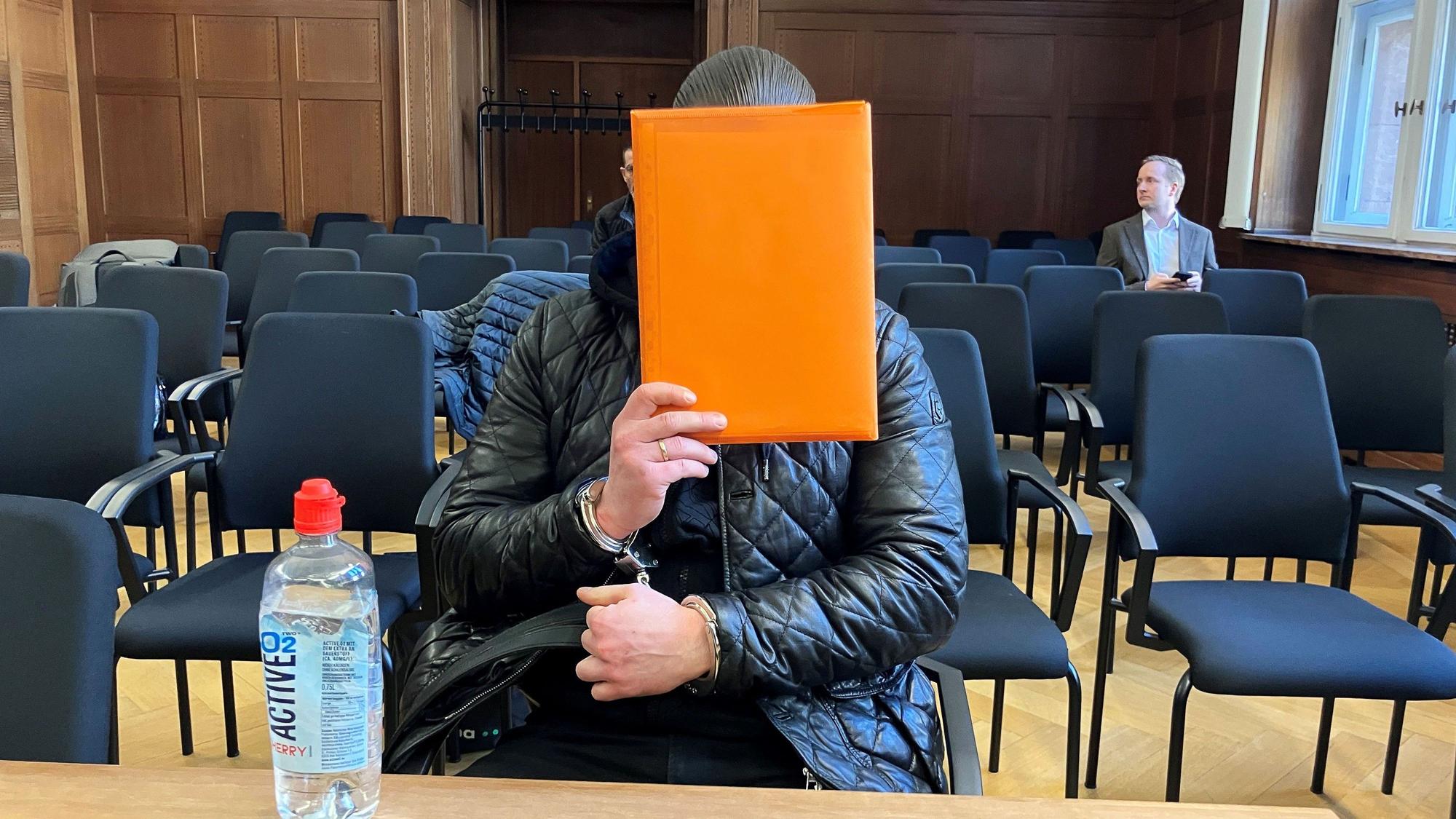 Der angeklagte Raser aus Duisburg sitzt im Verhandlungssaal und hält sich eine Mappe vor das Gesicht. Nach einem tödlichem Autorennen verhandelte das Verwaltungsgericht Düsseldorf über die Ausweisung des verurteilten Fahrers in den Kosovo.