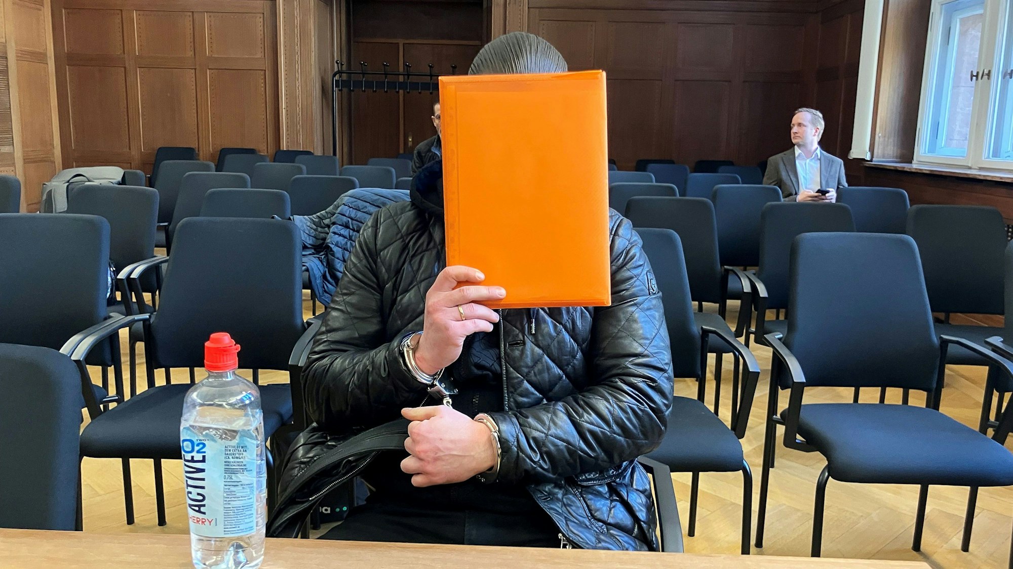 Der angeklagte Raser aus Duisburg sitzt im Verhandlungssaal und hält sich eine Mappe vor das Gesicht. Nach einem tödlichem Autorennen verhandelte das Verwaltungsgericht Düsseldorf über die Ausweisung des verurteilten Fahrers in den Kosovo.