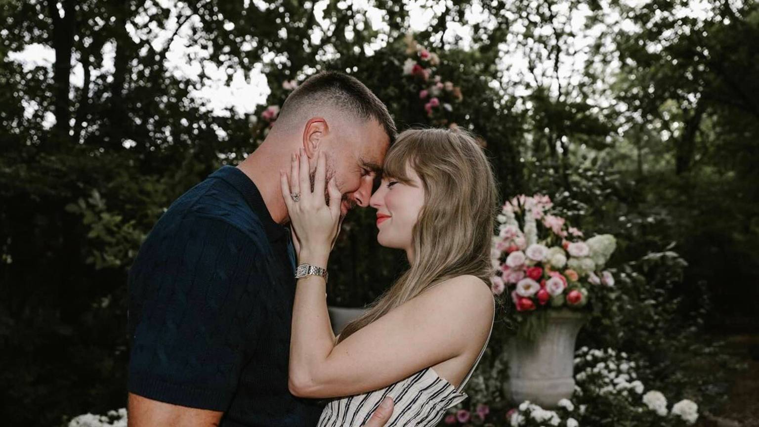 Travis Kelce und Taylor Swift umarmen sich vor einem Blumengesteck.