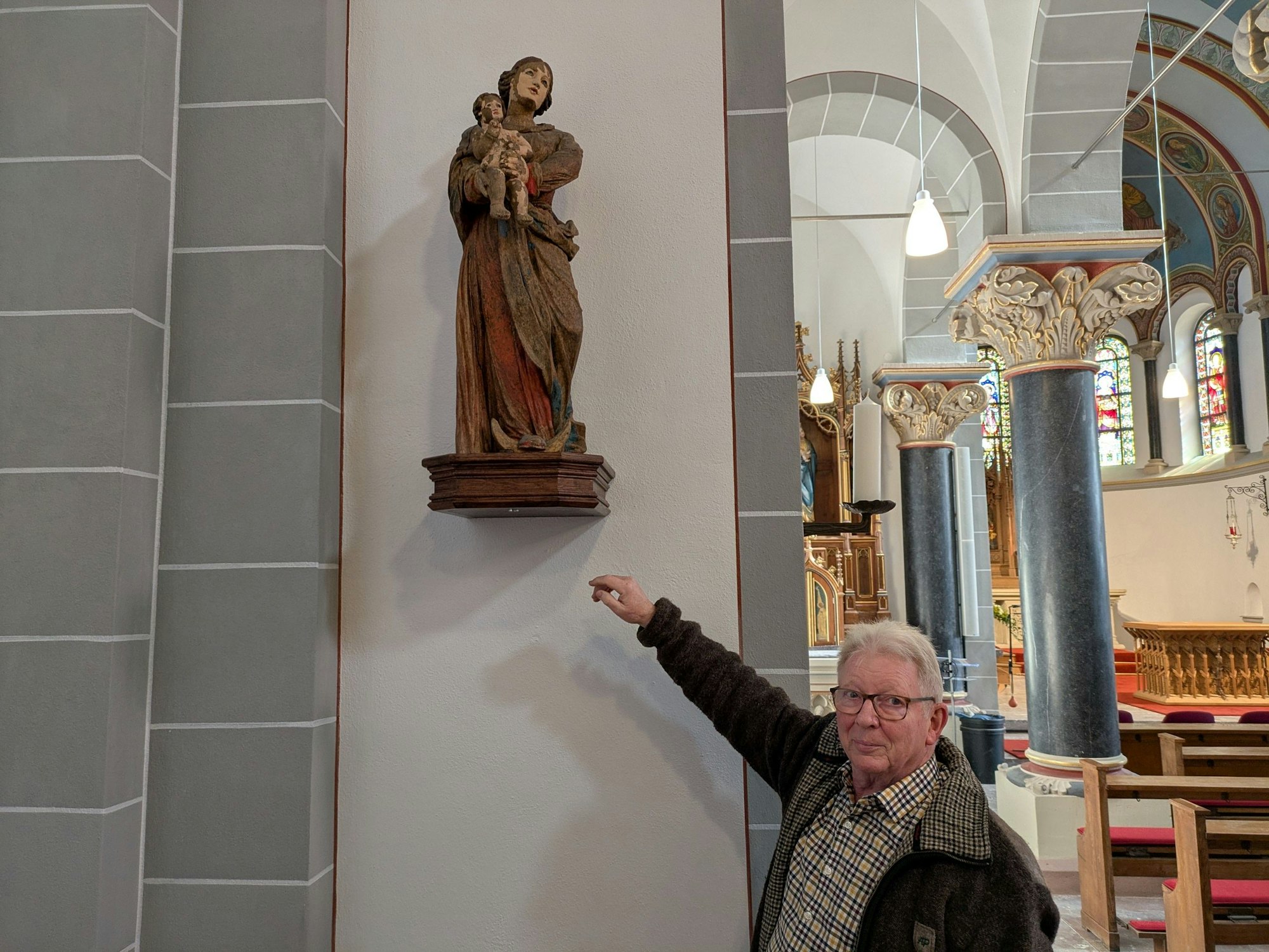 Ein Mann zeigt auf eine Marienstatue in einer Kirche.
