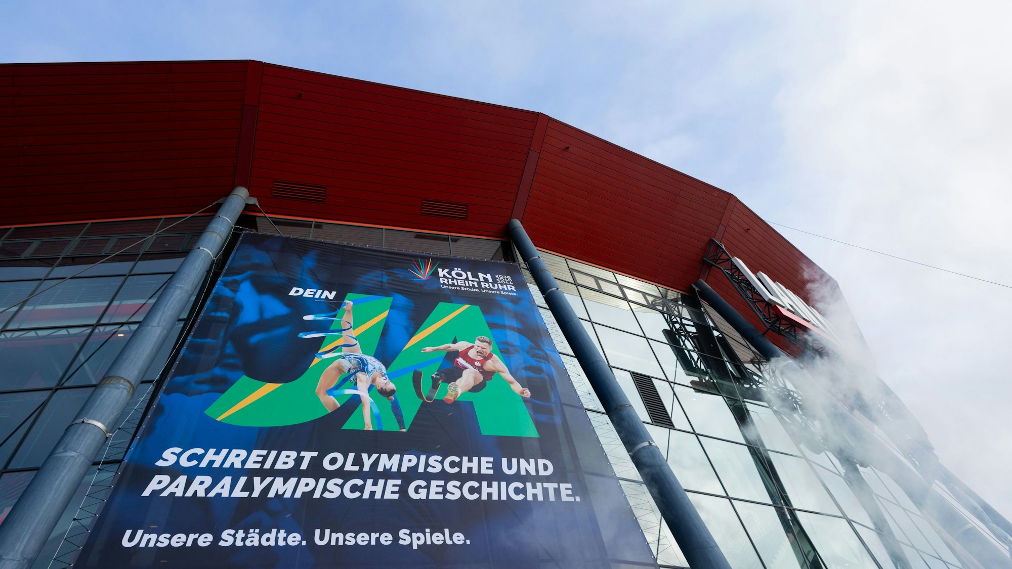 Ein Plakat mit dem Schriftzug „Ja“ wirbt an der Fassade der Lanxess-Arena für Olympische und Paralympische Spiele in Köln und der Region.