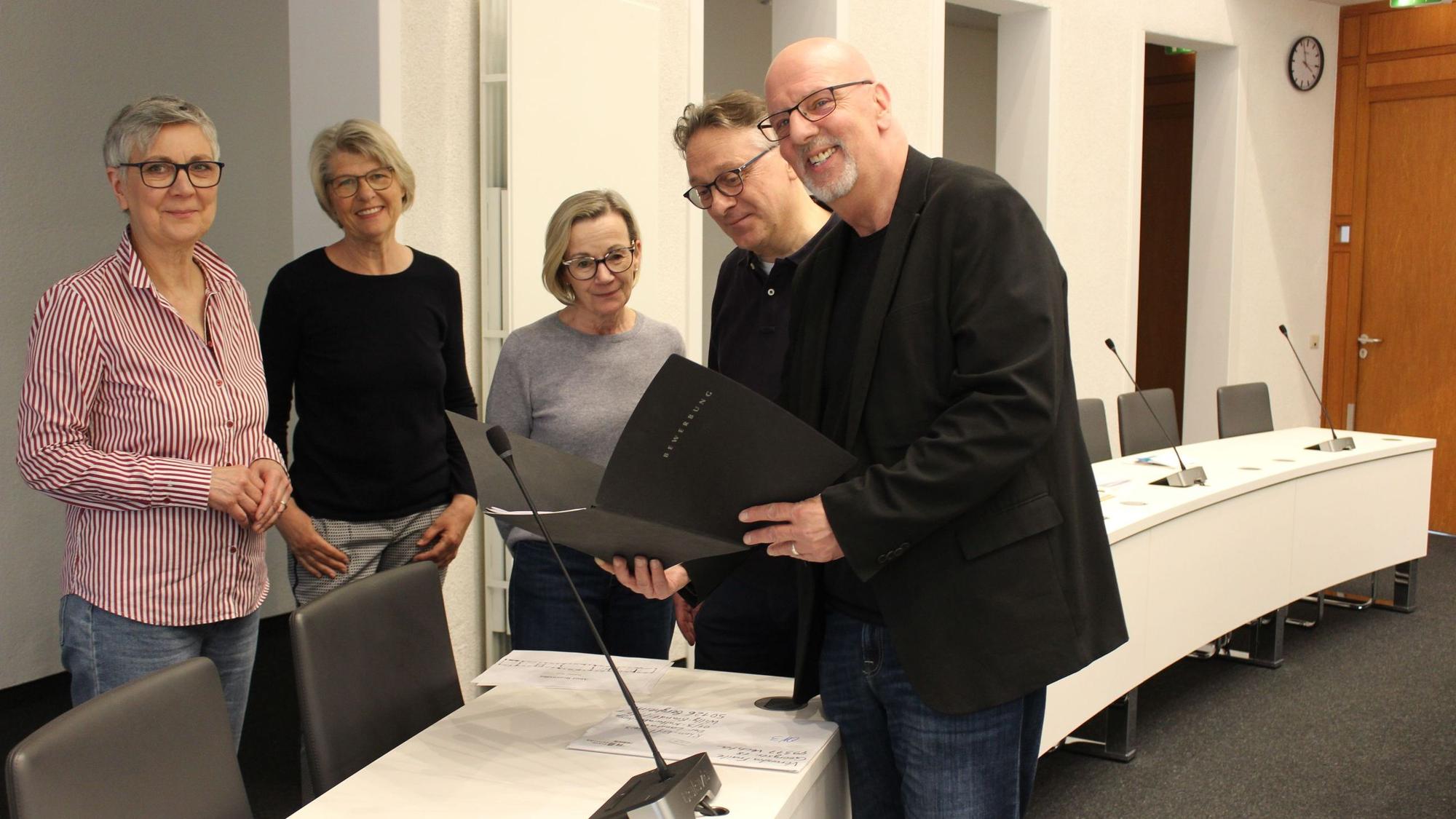 Männer und Frauen stehen an einem Tisch und halten schwarze Mappen.