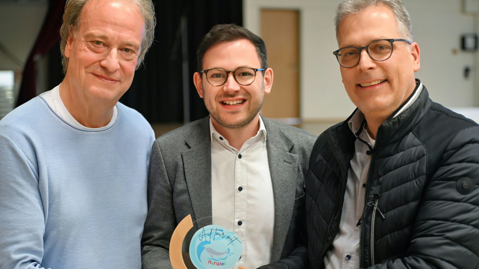 Die drei Männer stehen nebeneinander und präsentieren den Narwali-Pokal.