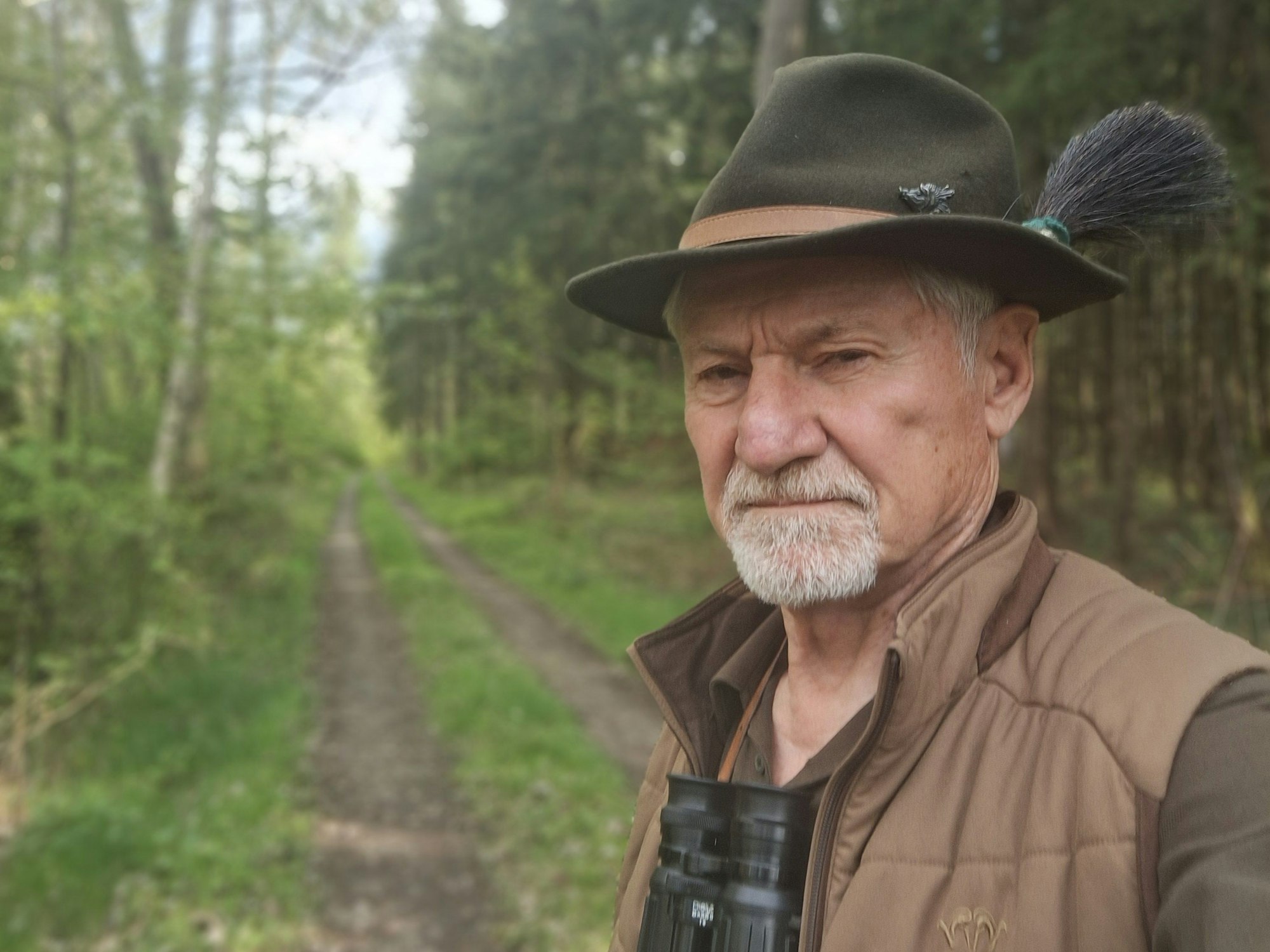 Das Foto zeigt den Jäger in Jagdmontur mit Fernglas in einem Waldstück.