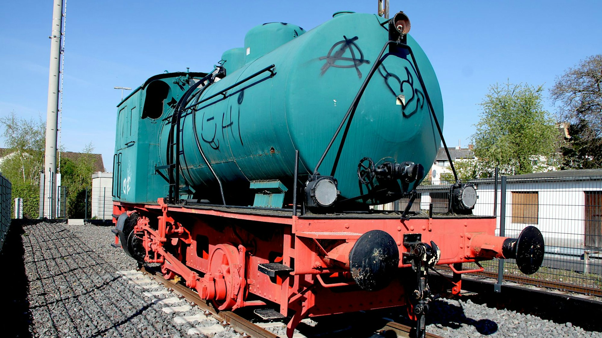 Eine türkise Lok steht auf einem Gleis.