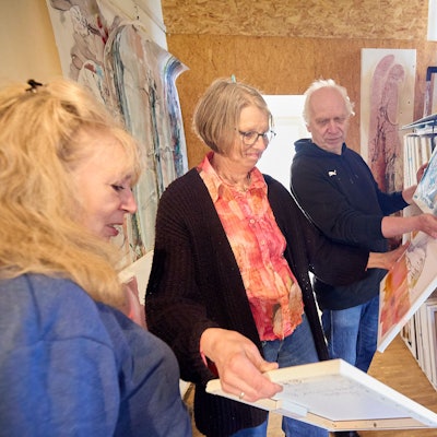 Gundolf und Marianne Roy und Maf Räderscheidt (v.r.n.l.) schauen sich in einem Atelier Gemälde an.