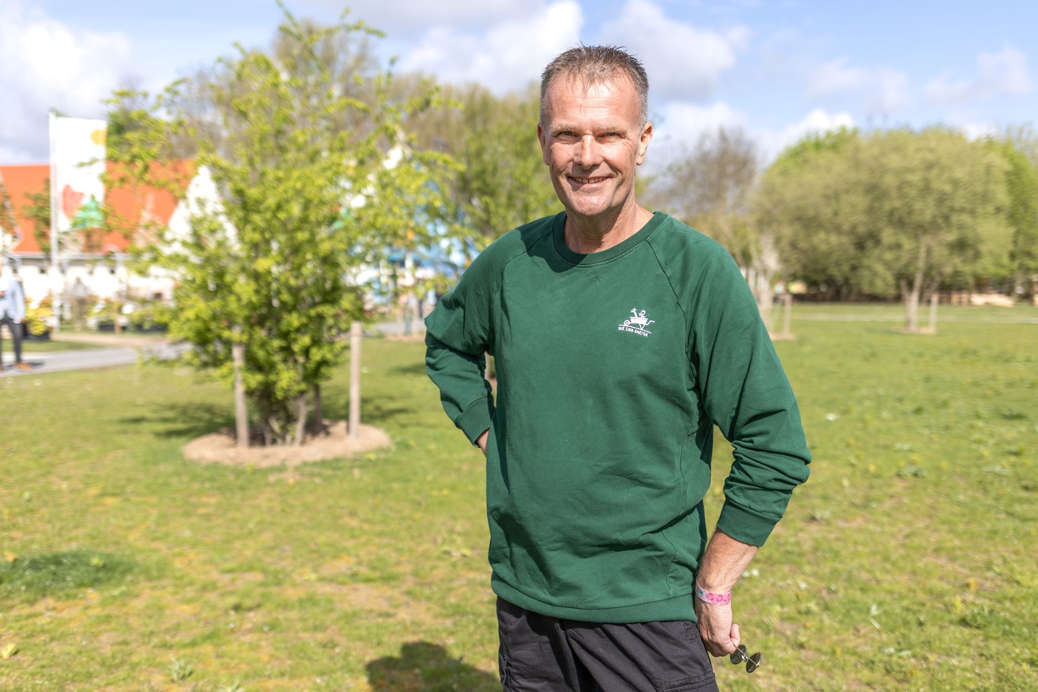 Ein Mann im grünen Pullover steht auf einer Wiese und schaut in die Kamera.