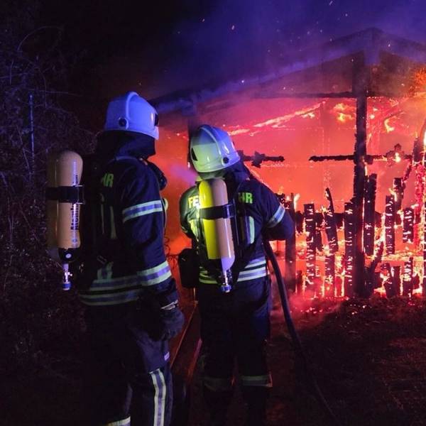 Feuerwehrleute löschen ein Holzhaus, das in voller Ausdehnung brennt.