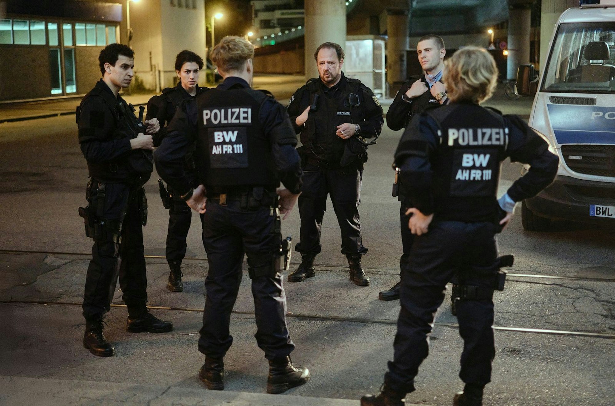 Sechs Bereitschaftspolizisten diskutieren, was sie in der Diskothek erlebt haben. Einsatzleiter Wolle Heizmann (Andreas Anke, dritter von links) ist sich uneins mit Mahmoud (Mouataz Alshaltouh, links), Mariam (Anna Bardavelidze, zweite von links), Jakub (Lasse Lehmann, dritter von links), Timo (Ben Felipe) und Pia (Caroline Hellwig). (Bild: SWR/Benoît Linder)