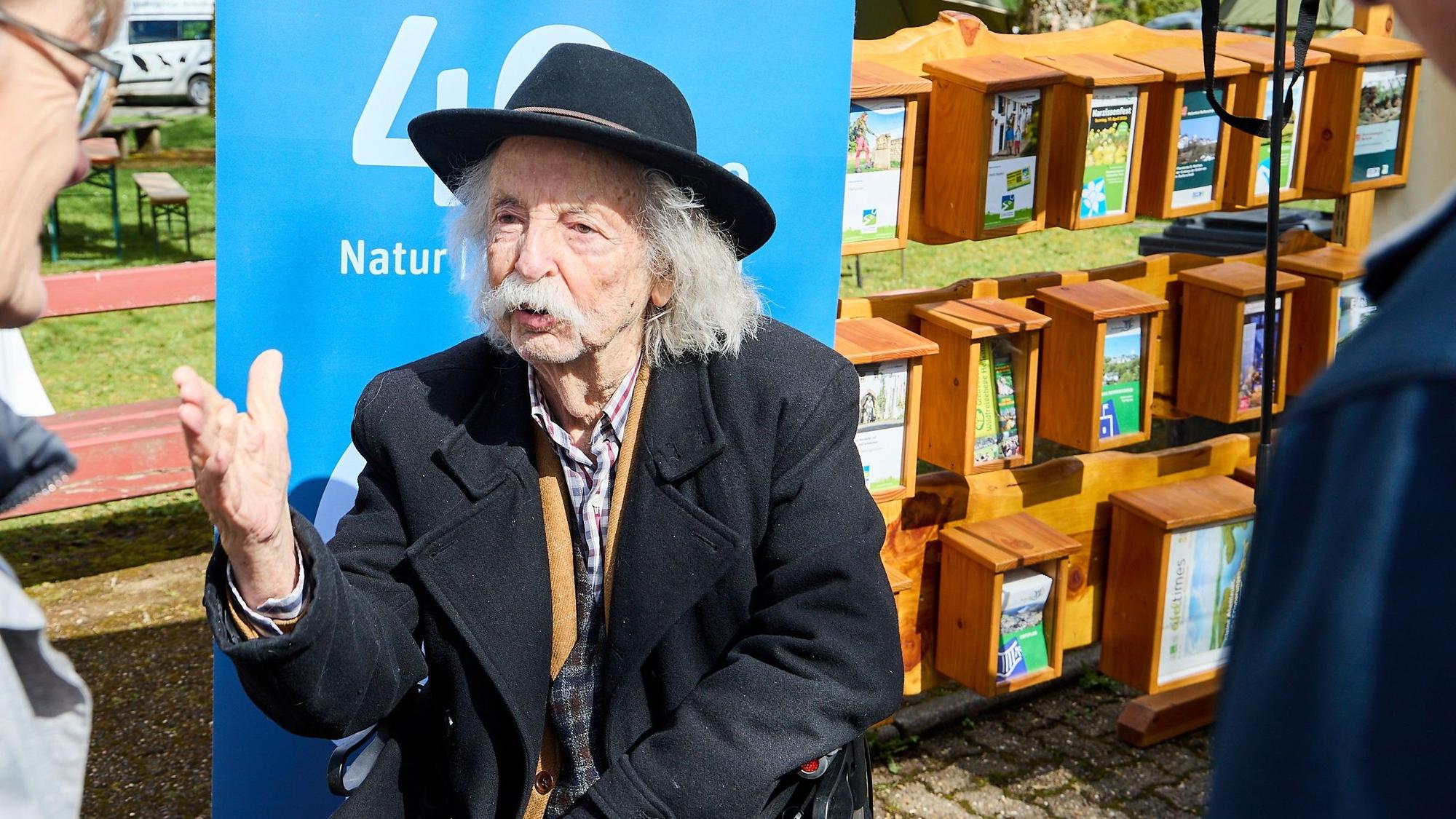 Jean Pütz sitzt auf einem Stuhl und gestikuliert mit einer Hand.