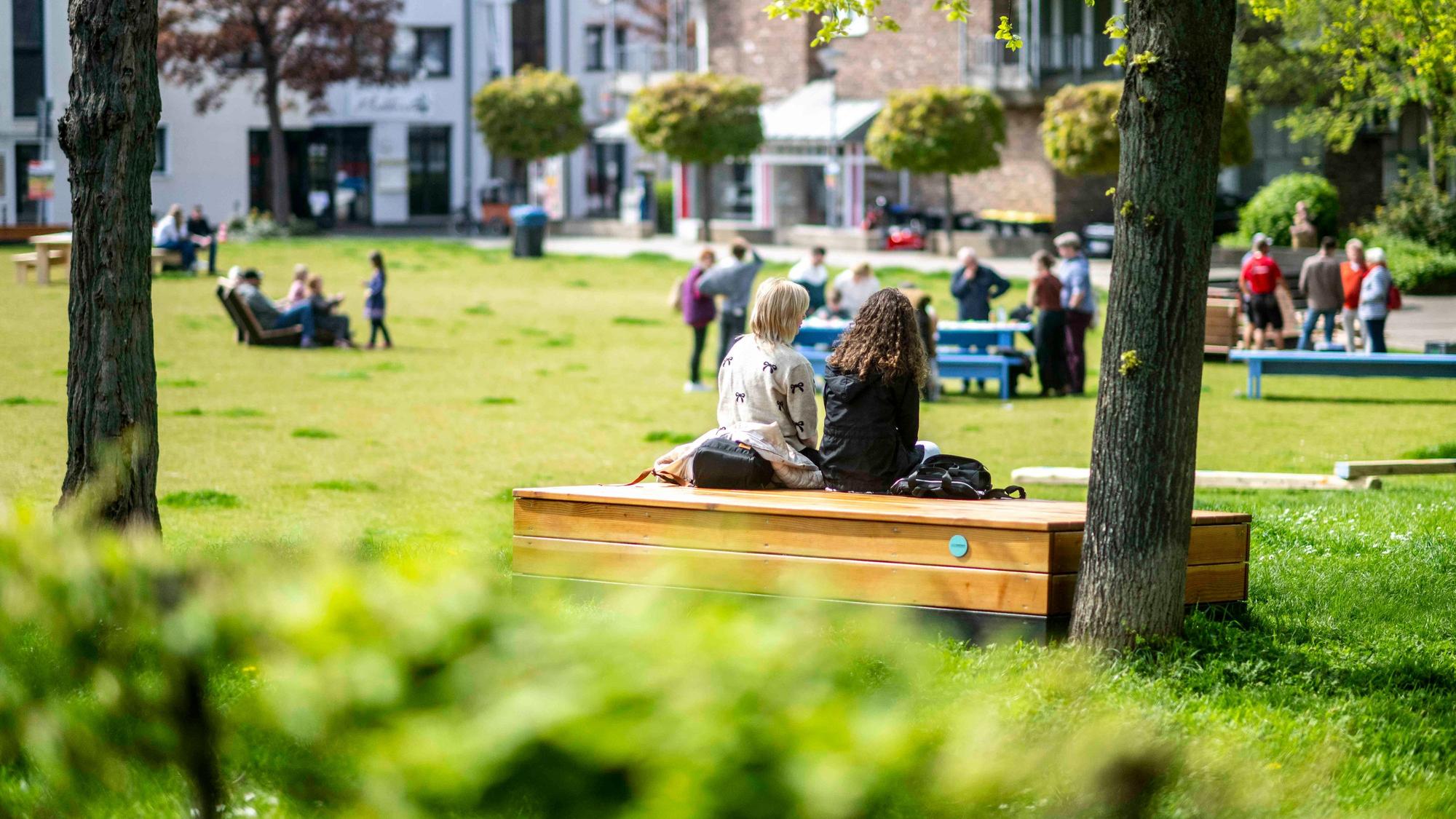 Das Bild zeigt einen Blick in den Klostergarten. Auf einer Sitzgelegenheit aus Holz haben zwei Frauen Platz genommen.