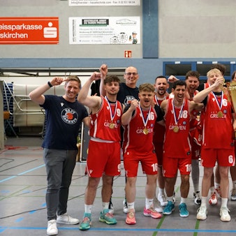 Die Erftbaskets Bad Münstereifel jubeln mit Landrat und Bürgermeister, zwei Spieler halten einen Pokal in die Höhe.