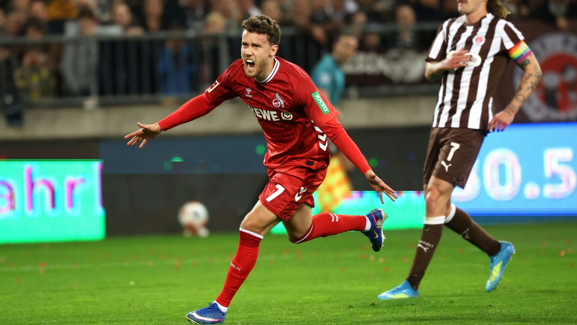 17.04.2026, Hamburg: Fußball, Männer: Bundesliga, FC St. Pauli - 1. FC Köln, 30. Spieltag, Millerntor-Stadion. Luca Waldschmidt (l, 1. FC Köln) jubelt nach einem 1:1 Ausgleichstreffer, während Jackson Irvine (FC. St. Pauli) zusieht. Foto: Christian Charisius/dpa - WICHTIGER HINWEIS: Gemäß den Vorgaben der DFL Deutsche Fußball Liga bzw. des DFB Deutscher Fußball-Bund ist es untersagt, in dem Stadion und/oder vom Spiel angefertigte Fotoaufnahmen in Form von Sequenzbildern und/oder videoähnlichen Fotostrecken zu verwerten bzw. verwerten zu lassen. +++ dpa-Bildfunk +++