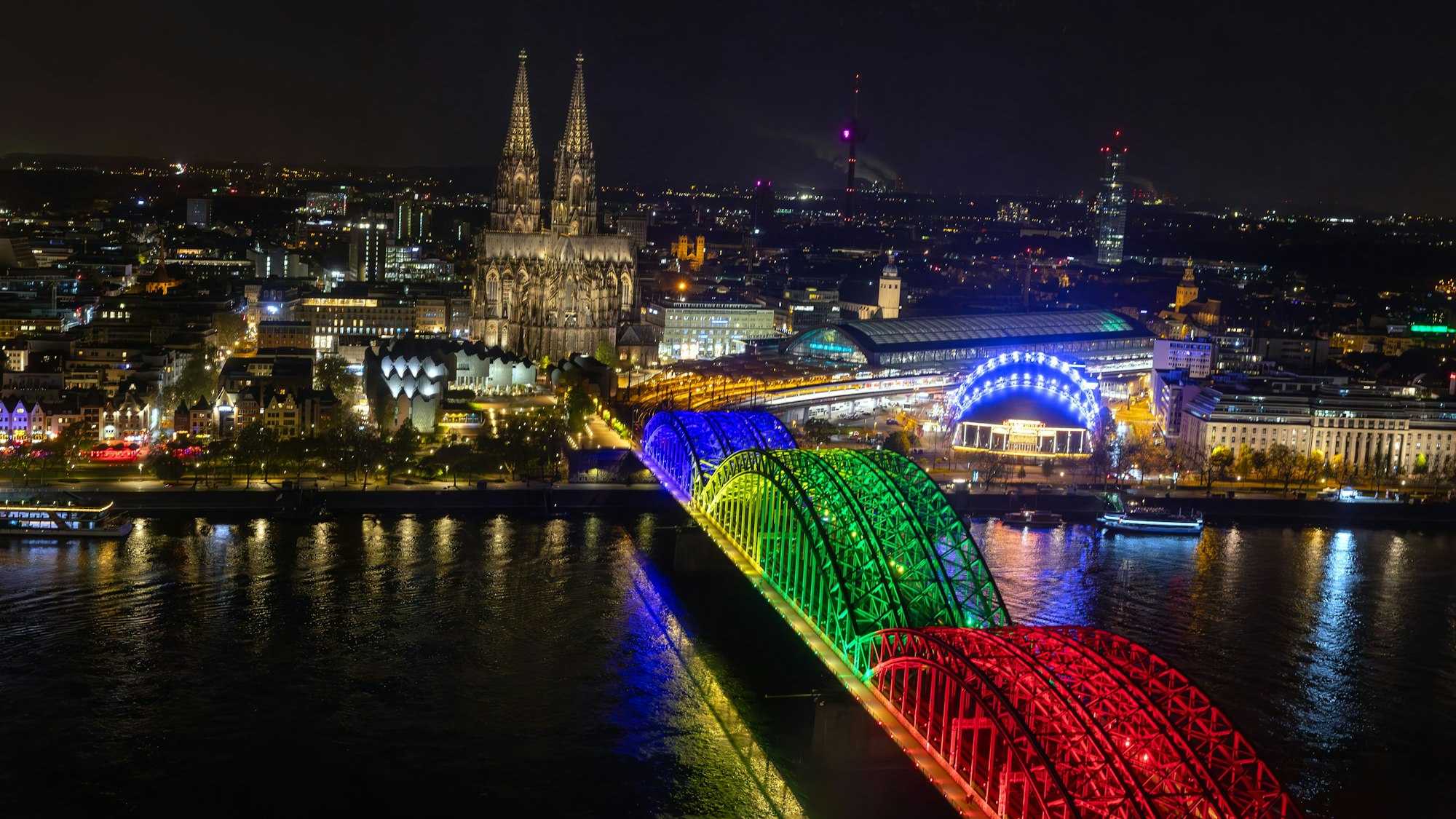 Die Bögen der Hohenzollernbrücke bunt beleuchtet in den Farben der olympischen Ringe.