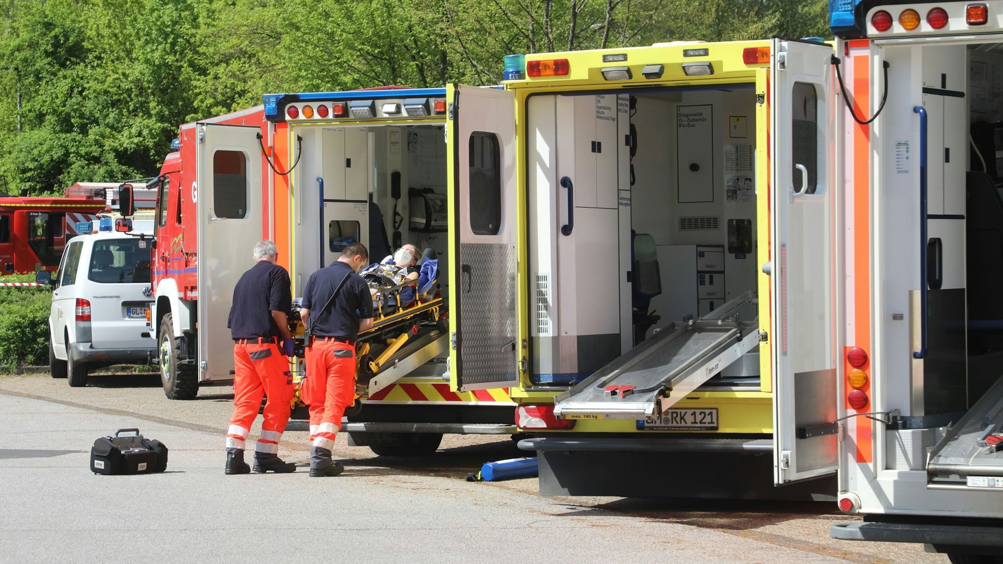 Rettungsassistenten schieben eine Trage mit einem Patienten in einen von mehreren nebeneinander stehenden Rettungswagen.