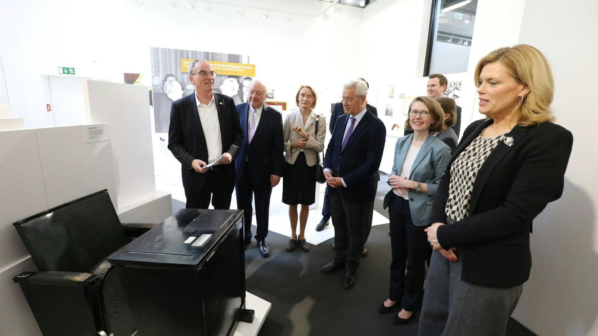Eine Gruppe von Männern und Frauen vor einem alten Bundestagsstuhl in einem Ausstellungsraum.