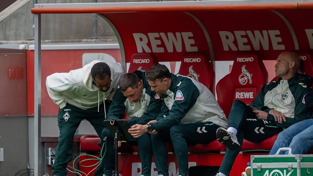 Bei einer Spielunterbrechung riskiert auch Trainer Daniel Thioune (l.) von Werder Bremen einen Blick auf das Tablet vor seiner Trainerbank.