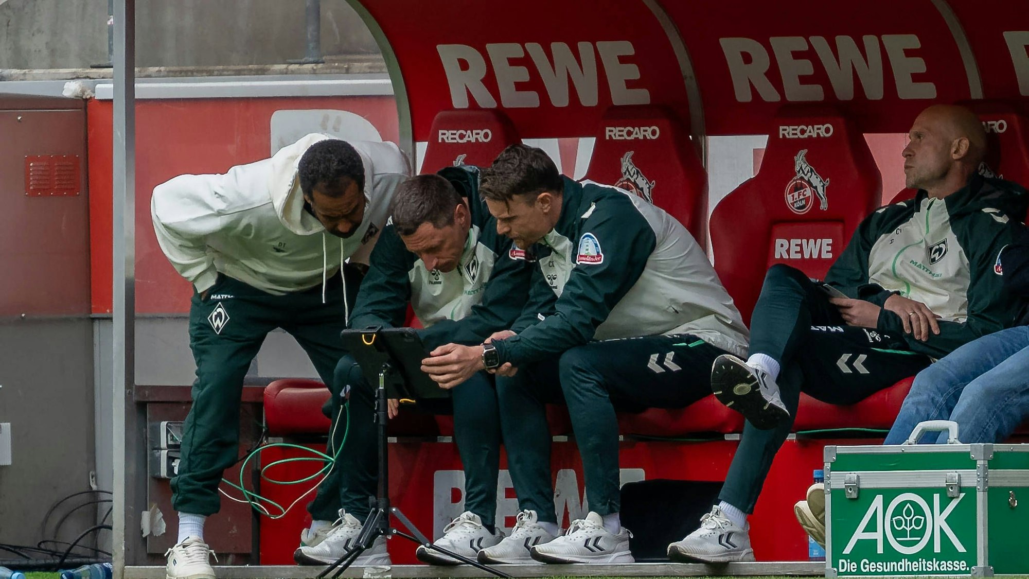 Bei einer Spielunterbrechung riskiert auch Trainer Daniel Thioune (l.) von Werder Bremen einen Blick auf das Tablet vor seiner Trainerbank.